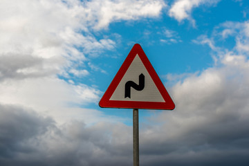 Double bend road sign against clearing sky after a heavy storm at sunset.