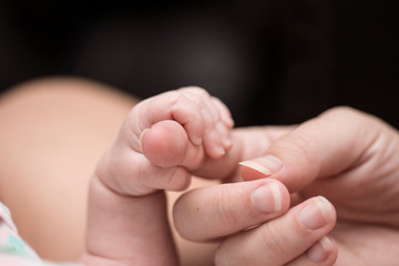Newborn baby holding finger of mother