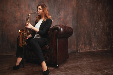 girl playing the saxophone sitting on the armchair. Copy space