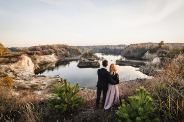 Young couple hugging people. A man and a woman standing near the lake. Look into the distance. Brides..Nature, forest, trees, grass. Career. Sunset. Standing between trees.