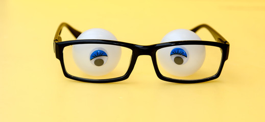 Black frame of glasses on a yellow background. Behind the glasses are tennis balls with glued pupils. Concept - eyes behind the glasses of glasses, expressing fear, confusion, thoughtfulness. Observat