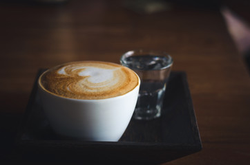 close up modern hot black coffee the cappuccino on wood background with coffee bubble foam pattern and texture in white cup looking and feel so delicious on glasses table in coffee shop.