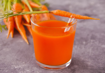 Carrot juice and young carrots in glass on concrete background