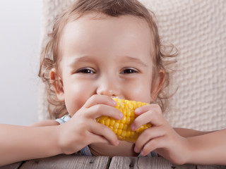 little curly cute girl eating corn sitting on the chair.