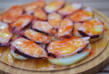 Grilled octopus tentacle slices with pimento paprika powder and sliced potato on round wood plate close up view