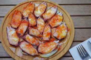Grilled octopus tentacle slices with pimento paprika powder and sliced potato on round wood plate top view