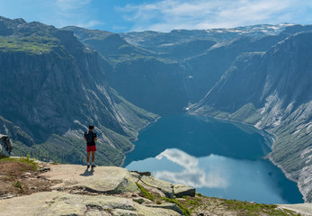 Naklejka premium Mountain lake landscape, Norway. Young man standing on the shore of Ringedalsvatnet lake. Way to Trolltunga rock.