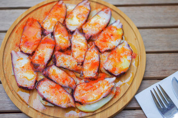 Octopus tentacle slices with crab roe and sliced potato on round wood plate top view