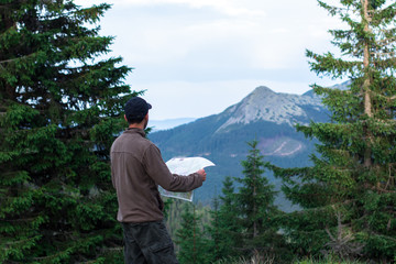 Fototapeta na wymiar hiker man in cap with map in front of mountain range in the carpathian mountains gorgany