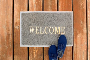 Welcome is written on the rug and shoes are standing nearby
