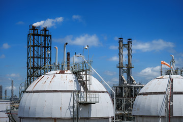 Close up of Gas storage sphere tanks and smoke stack in petrochemical industry or oil and gas refinery plant on blue sky with white cloud
