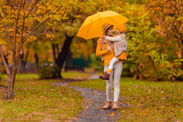 Obraz premium mom holds daughter in her arms under a yellow umbrella in the park in autumn