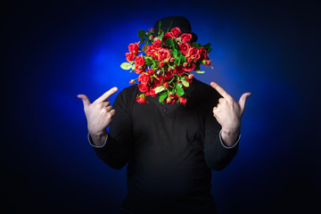 The man's face is covered with flowers. A guy and a bunch of red roses. A man chooses a gift. The wizard conjured a bouquet. Congratulations on women's day. Witchcraft. A gift for the holiday