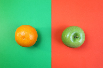fruits orange and green apple lie on the halves of multi-colored paper