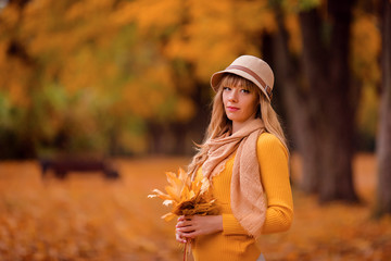 beautiful woman in a brown hat with a bouquet of autumn leaves for a walk in the park