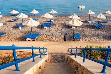 Island of Cyprus. Pissouri. Empty beach on the Mediterranean coast. Sandy beach with sunbeds and umbrellas. Rest on the Mediterranean. Stairs lead to the beach.