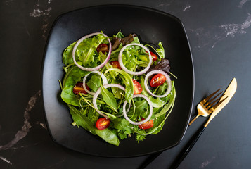 Eat green concept with organic fresh vegetable salad in ceramic plate on black background.
