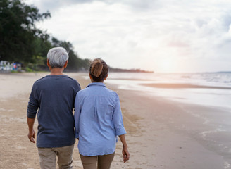 Mature couples relax at the seaside on holiday.An elderly couple walking on the beach to relax on vacation.Elderly couple standing on the beach holding hands.