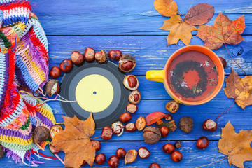 Yellow ceramic cup of herbal tea and vinyl records on aged wooden background with fall autumn leaves and chestnuts.