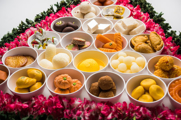 Fototapeta na wymiar Flower Rangoli with sweets/mithai and diya in bowls for Diwali or any other festivals in India, selective focus