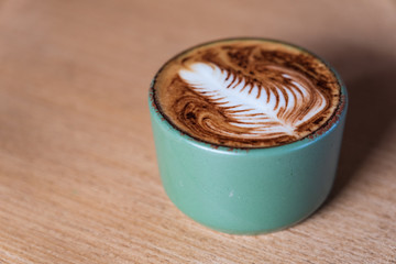 Cappuccino coffee with latte art milky foam on wooden table background.