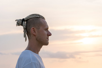 Silhouette of a young guy with dreadlocks on his head near sea during sunset. Close up portrait