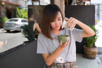 Pretty female tourists pouring milk into green coffee mug outside the coffee shop.