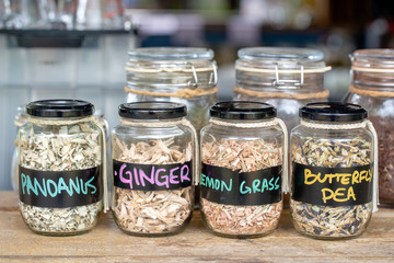 Assortment of dried spices in glass bottles on wooden background. Dry ginger, pandanus, lemon grass and butterfly pea in glass jars