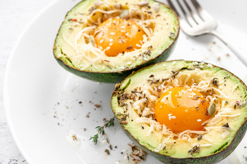 Tasty and healthy avocado snack. Slices of avocado with raw yolk, cheese, olive oil and spices on a white plate close-up.