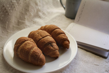 .breakfast with coffee and croissants, on a light background with a notebook