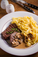 Grilled beef steaks and noodles in creamy mushroom sauce, garnished with thyme on white plate