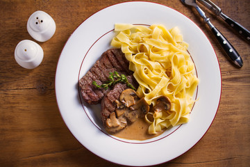 Grilled beef steaks and noodles in creamy mushroom sauce, garnished with thyme on white plate