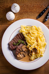 Grilled beef steaks and noodles in creamy mushroom sauce, garnished with thyme on white plate