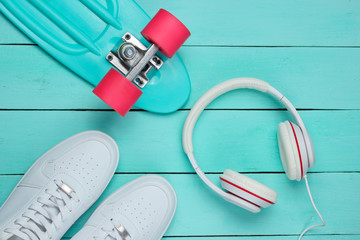 Hipster outfit. Skateboard with headphones and sneakers on blue wooden background. Creative fashion minimalism. Minimal summer fun. Pop art. 80s. Music concept. Top view