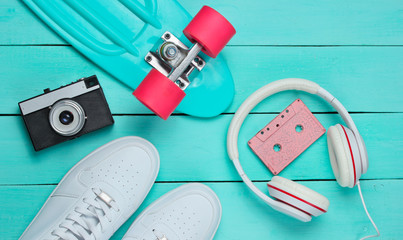 Hipster outfit. Skateboard, headphones, audio cassette, sneakers, retro camera on blue wooden background. Creative fashion minimalism. Minimal summer fun. Pop art. 80s. Copy space. Top view