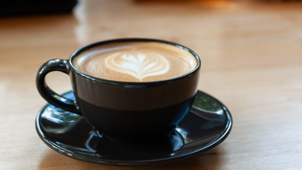 Latte art coffee in black cup set on wooden table, beverage art by fresh milk with coffee.