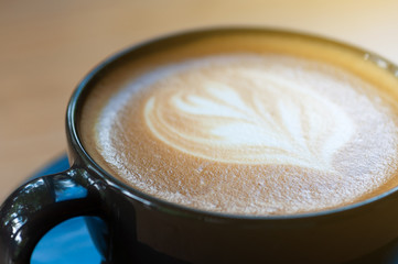 Latte art coffee in black cup set on wooden table, beverage art by fresh milk with coffee.