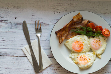 scrambled eggs, bacon, tomatoes and cutlery on a white table