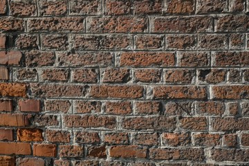 Texture of old red brick wall, illuminated by the sun. In corner some new brick to repair wall.