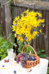 bouquet of flowers, wine, glasses and grapes against the background of an old fence