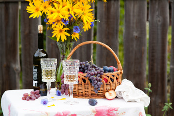 bouquet of flowers, wine, glasses and grapes against the background of an old fence