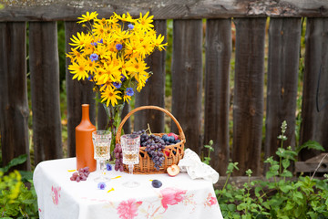 bouquet of flowers, wine, glasses and grapes against the background of an old fence