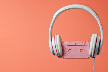 White classic wired headphones with audio cassette isolated on coral color background. Retro style. 80s. Minimalistic music concept.