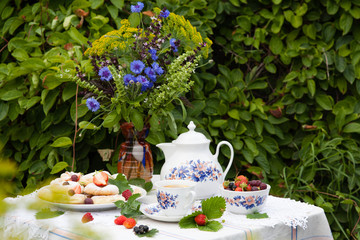 Still life with bouquet of flowers, tea, cookies and berries on table in garden