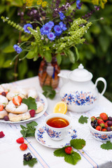 Still life with bouquet of flowers, tea, cookies and berries on table in garden