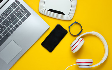 Modern digital gadgets and accessories. Laptop, smartphone, smart bracelet, headphones, wi-fi router on a yellow background. Top view.