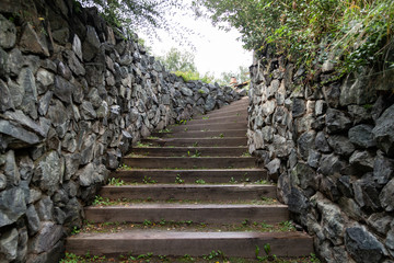 A long high staircase with wooden steps extending upward surrounded by stone walls in summer. Travel and mystical places.