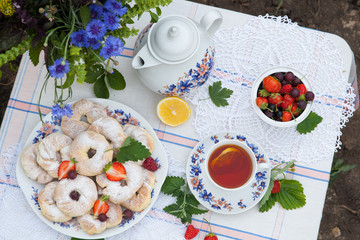 Still life with bouquet of flowers, tea, cookies and berries on table in garden