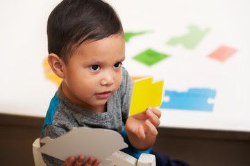 A smart latino boy choosing the correct colored shape from a table and showing it to the preschool teacher.