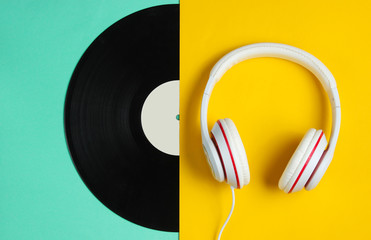 Retro style music concept. Classic headphones, half  vinyl record on colored paper background. Pop culture. 80s. Top view